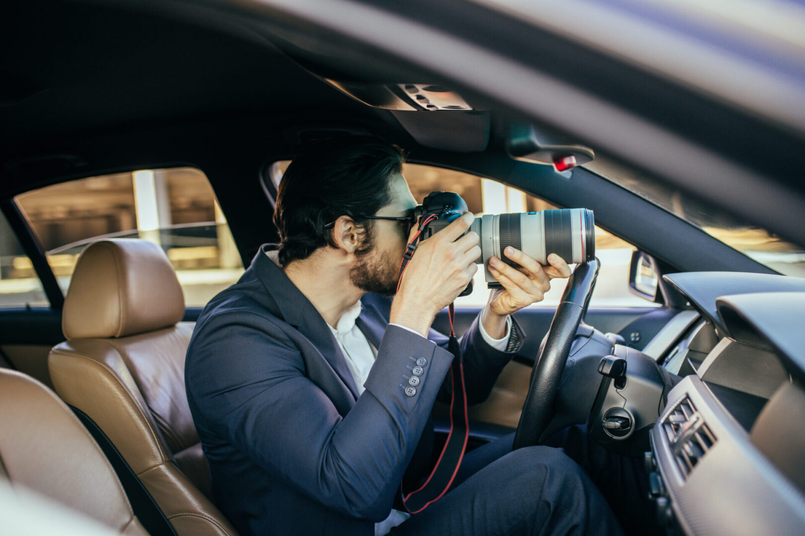 A man sitting in the driver 's seat of his car while holding two cell phones.